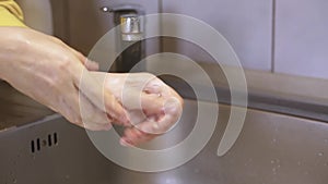 Unknown person washing hands under faucet, using soap from white liquid soap despenser, trying to wash off microbes, washing hands