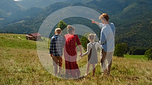 Family walking down green mountain hill back view. Parents with kids relax.