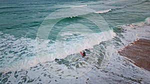 Unknown surfer entering ocean holding surfboard at stormy waves aerial view