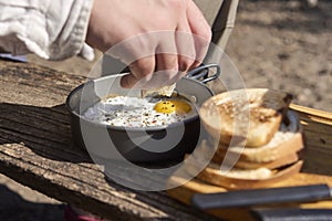 Unknown traveler eating breakfast outdoors, fried eggs and toasted bread slices