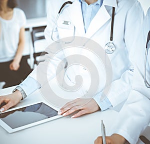 Unknown two woman-doctors at work with patient at the background. Female physicians filling up medical documents at