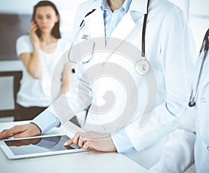 Unknown two woman-doctors at work with patient at the background. Female physicians filling up medical documents at