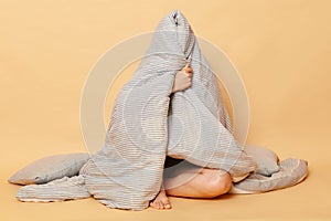Unknown unrecognizable woman sitting on floor wrapped in plaid wearing pajama, sleep eye mask isolated over beige background