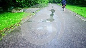 Unknown woman cycling along park road after summer rain