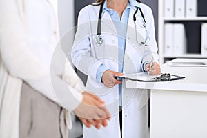 Unknown woman doctor and female patient discussing something while standing near reception desk in emergency hospital