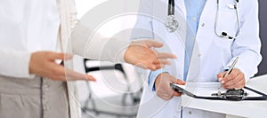 Unknown woman doctor and female patient discussing something while standing near reception desk in emergency hospital