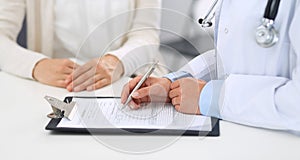 Unknown woman doctor and female patient discussing something while standing near reception desk in emergency hospital