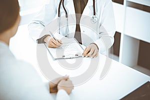 Unknown woman-doctor and female patient sitting and talking at medical examination in clinic, close-up. Therapist
