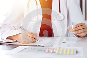 Unknown woman-doctor fills up prescription form in sunny room, close-up