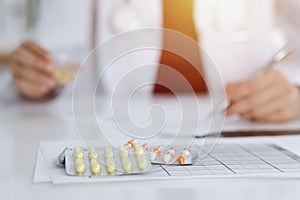 Unknown woman-doctor fills up prescription form in sunny room, close-up