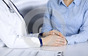 Unknown woman-doctor is holding her patient`s hands to reassure a patient, while sitting together at the desk in the