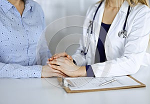 Unknown woman-doctor is holding her patient`s hands to reassure a patient, while sitting together at the desk in the