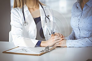 Unknown woman-doctor is holding her patient& x27;s hands to reassure a patient, while sitting together at the desk in the