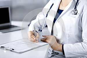 Unknown woman-doctor is prescribing some medication for her patient, using a clipboard, while sitting at the desk in her