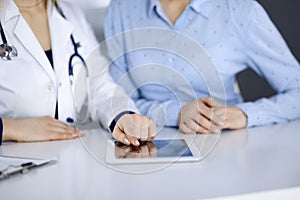 Unknown woman-doctor is showing to her patient a description of medication, while sitting together at the desk in the