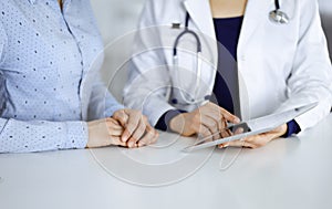 Unknown woman-doctor is showing to her patient a description of medication, while sitting together at the desk in the