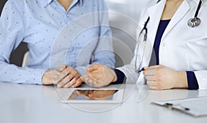 Unknown woman-doctor is showing to her patient a description of medication, while sitting together at the desk in the