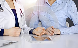 Unknown woman-doctor is showing to her patient a description of medication, while sitting together at the desk in the