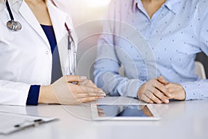 Unknown woman-doctor is showing to her patient a description of medication, while sitting together at the desk in the