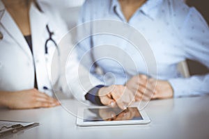 Unknown woman-doctor is showing to her patient a description of medication, while sitting together at the desk in the