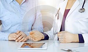 Unknown woman-doctor is showing to her patient a description of medication, while sitting together at the desk in the