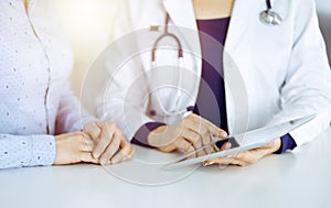 Unknown woman-doctor is showing to her patient a description of medication, while sitting together at the desk in the