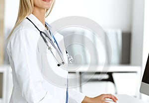 Unknown woman-doctor is typing on desktop computer at reception desk in clinic. Physician at work, close-up. Medicine