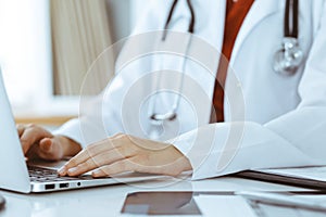 Unknown woman-doctor typing on laptop computer while sitting at the table. Medicine concept