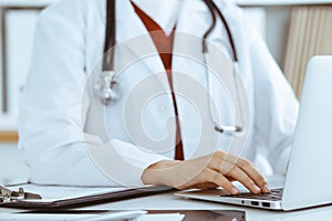 Unknown woman-doctor typing on laptop computer while sitting at the table. Medicine concept