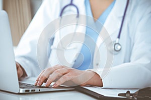 Unknown woman-doctor typing on laptop computer while sitting at the table. Medicine concept