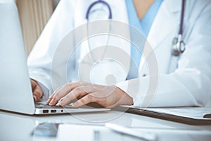 Unknown woman-doctor typing on laptop computer while sitting at the table. Medicine concept