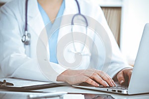 Unknown woman-doctor typing on laptop computer while sitting at the table. Medicine concept