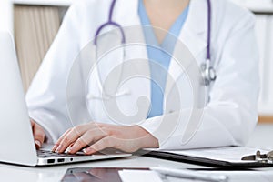 Unknown woman-doctor typing on laptop computer while sitting at the table. Medicine concept