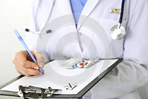 Unknown woman doctor at work at hospital. Pills at medical clipboard. Young female physician write prescription or
