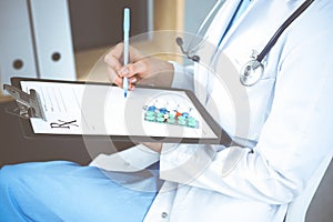 Unknown woman doctor at work at hospital. Pills at medical clipboard. Young female physician write prescription or