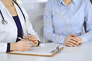 Unknown woman-doctor is writing down on her papers patient`s symptoms of a cold, while sitting together at the desk in
