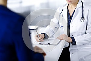 Unknown woman-doctor is writing some medical recommendations to her patient, while they are sitting together at the desk