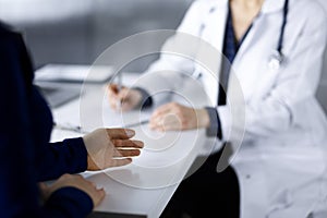 Unknown woman-doctor is writing some medical recommendations to her patient, while they are sitting together at the desk