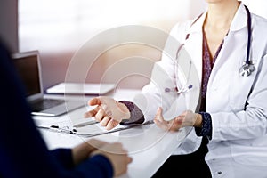 Unknown woman-doctor is writing some medical recommendations to her patient, while they are sitting together at the desk