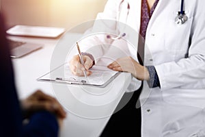 Unknown woman-doctor is writing some medical recommendations to her patient, while they are sitting together at the desk