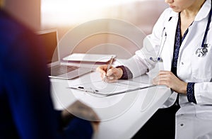 Unknown woman-doctor is writing some medical recommendations to her patient, while they are sitting together at the desk