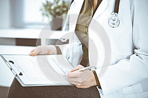 Unknown woman-doctor writing something at clipboard while sitting at the chair, close-up. Therapist wearing green blouse