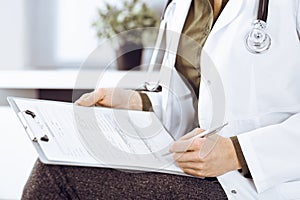 Unknown woman-doctor writing something at clipboard while sitting at the chair, close-up. Therapist wearing green blouse