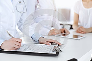 Unknown woman-doctors at work consulting patient. Female physicians filling up medical documents or prescription, close