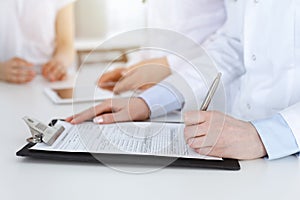 Unknown woman-doctors at work consulting patient. Female physicians filling up medical documents or prescription, close