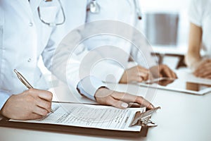 Unknown woman-doctors at work consulting patient. Female physicians filling up medical documents or prescription, close