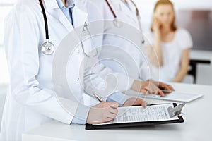 Unknown woman-doctors at work with patient at the background. Female physicians filling up medical documents or