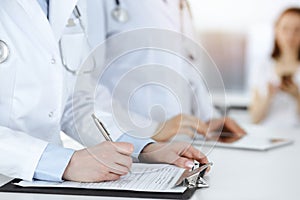 Unknown woman-doctors at work with patient at the background. Female physicians filling up medical documents or