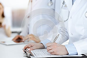 Unknown woman-doctors at work with patient at the background. Female physicians filling up medical documents or