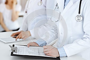 Unknown woman-doctors at work with patient at the background. Female physicians filling up medical documents or